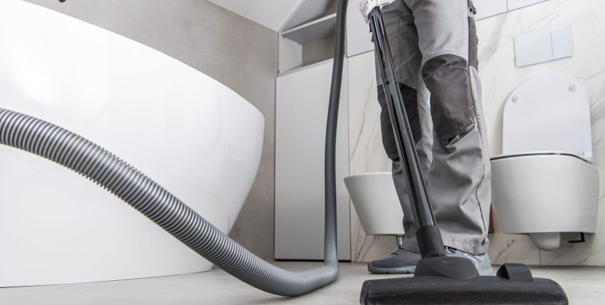 Man Vacuuming White Tile Floor In Bathroom. Caucasian Male Cleaning And Vacuuming Tile Floor In Newly Remodeled Residential Bathroom.