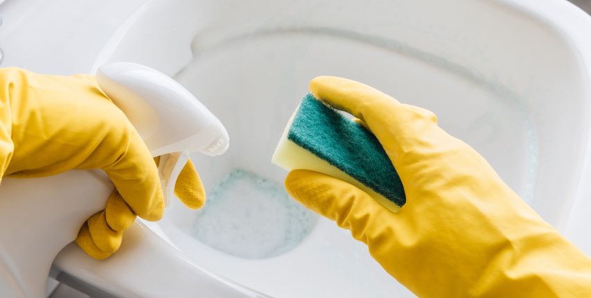 Woman in yellow rubber gloves cleaning toilet with detergent Woman in yellow rubber gloves cleaning toilet bowl with detergent